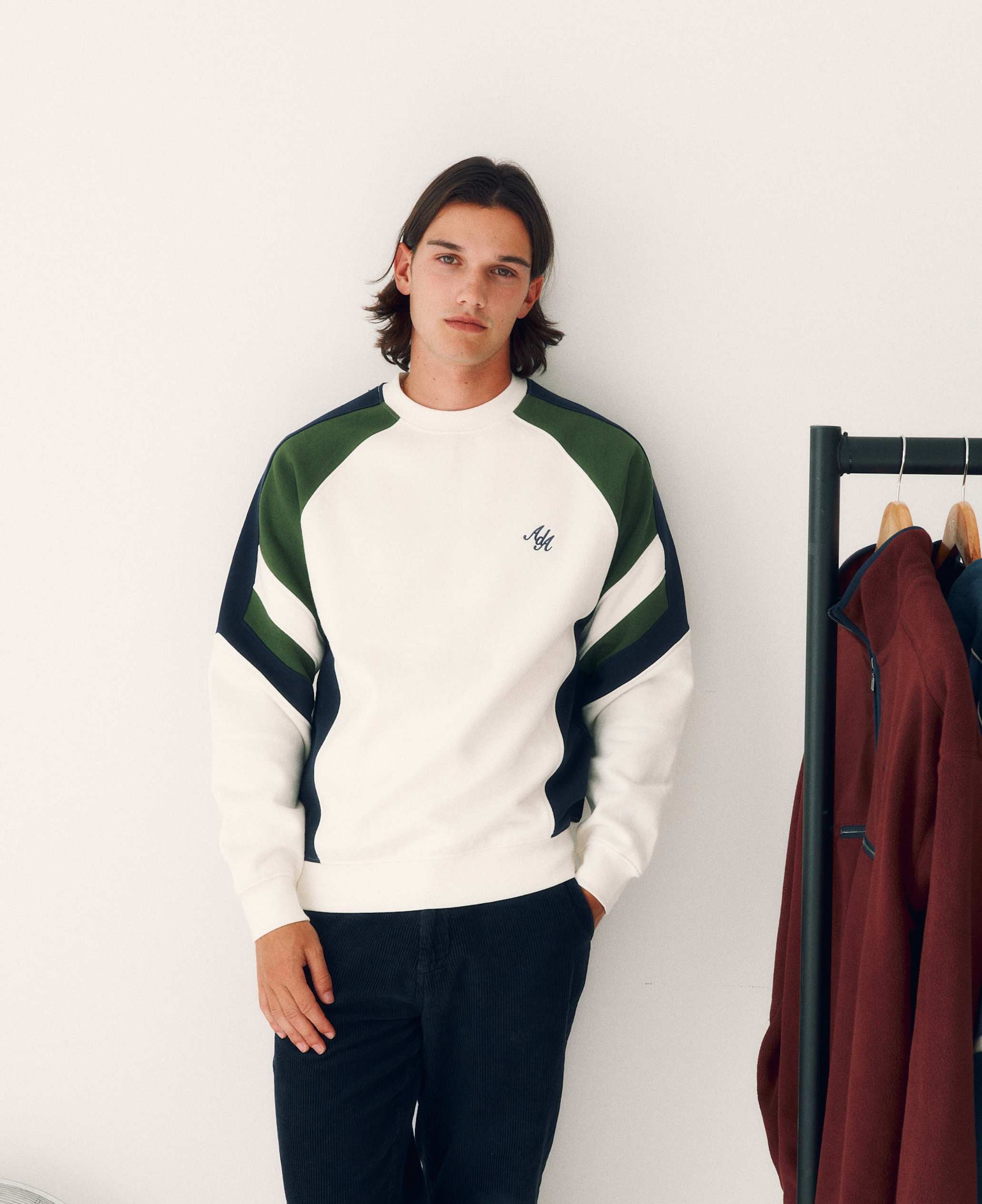 Person wearing a green and white sweater with a brand logo, standing against a plain background.