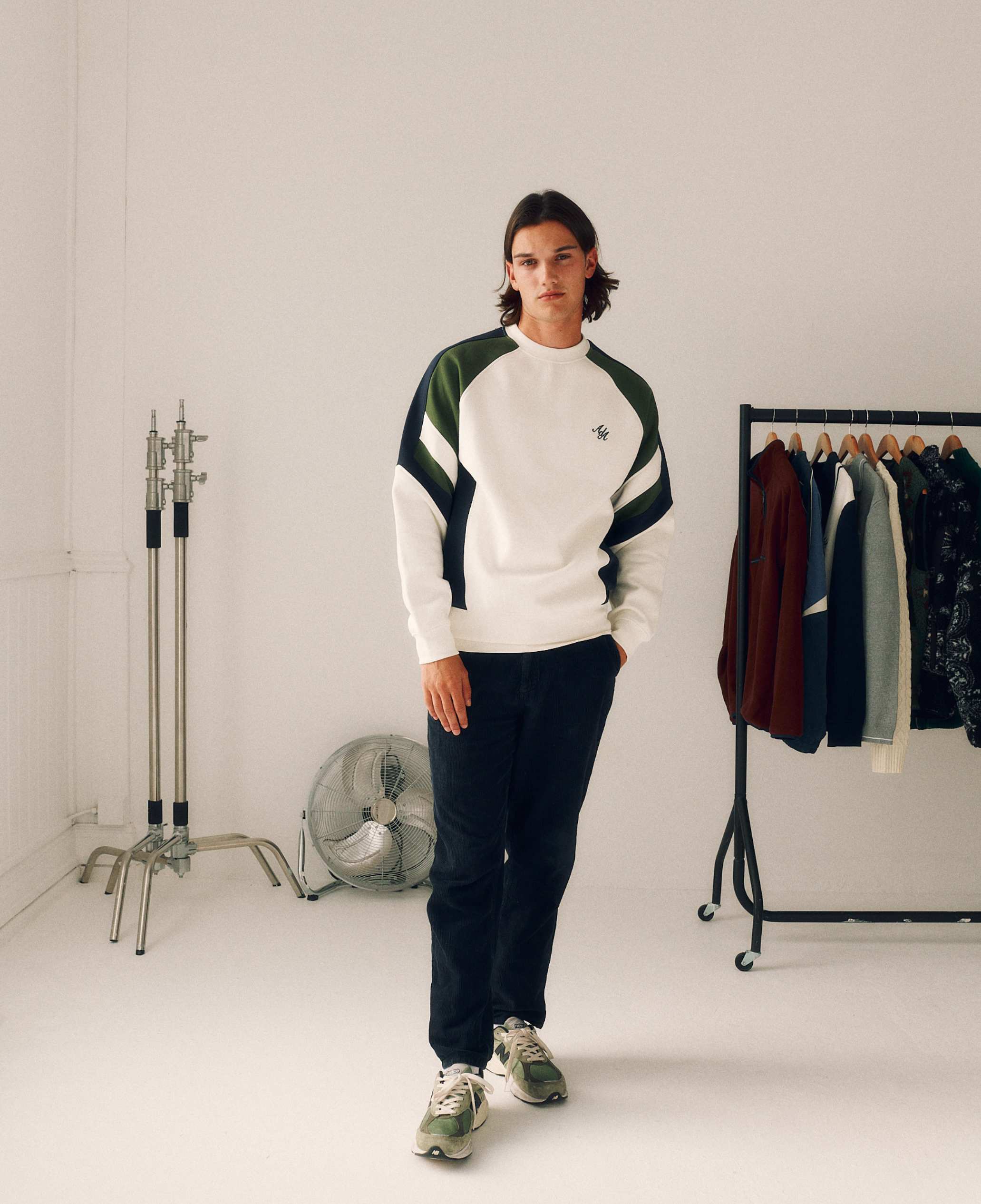 Person wearing a green, white, and navy sweater with dark pants in a room with clothing racks.